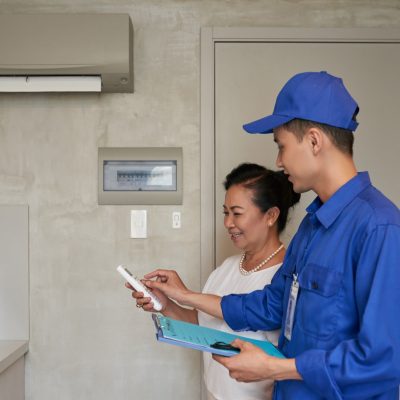 Technician explaining senior Vietnamese woman how to use air conditioner