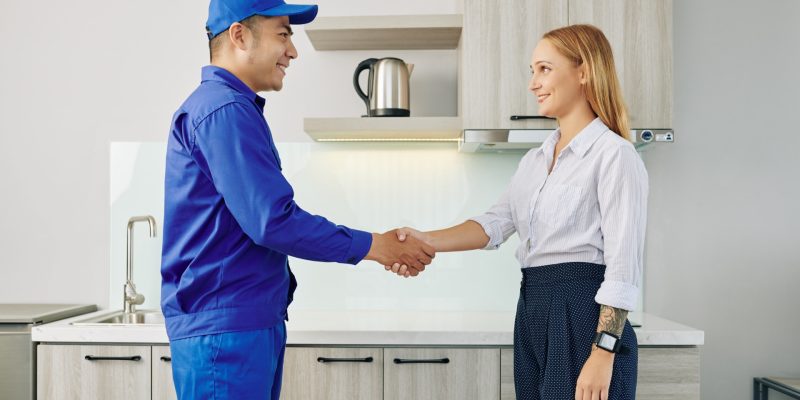 Positive pretty young woman shaking hand of repairman after he finished work