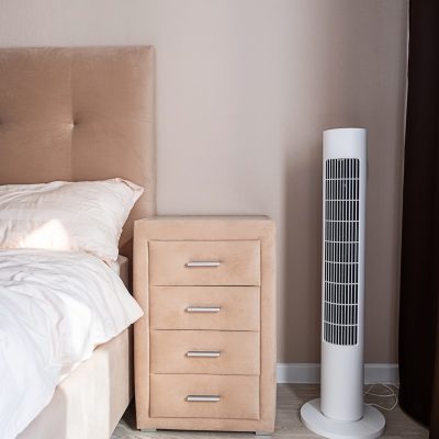 Modern bedroom with sleek tower fan and beige nightstand.